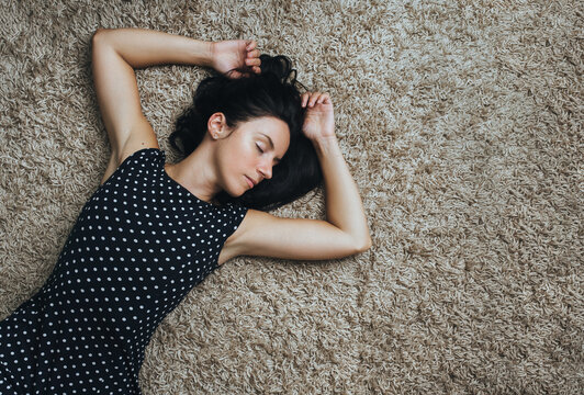 A young Caucasian black-haired girl in a polka-dot sundress lies on a carpet with a high pile and rests. Daytime sleep, relaxation and rest. view from above.