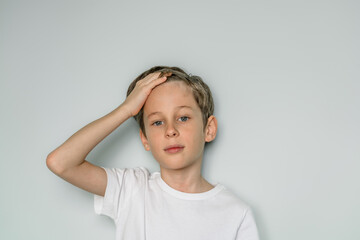 Portrait of a nine-year-old white boy on the background of a white wall straightens his hair on his head