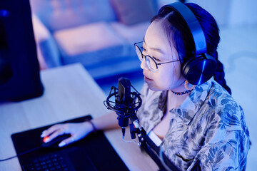 High angle portrait of young teenage girl playing video game on PC and speaking to microphone while...