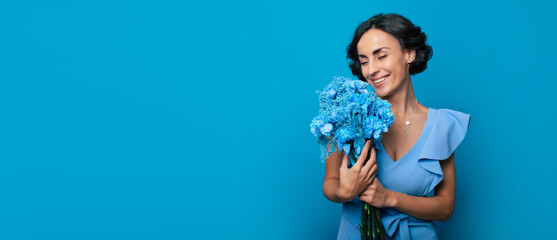 The portrait of a happy excited gorgeous young woman in an elegant blue dress is posing with a fresh bunch of blue flowers. Mothers day. Women's holidays. Springtime. Women rights