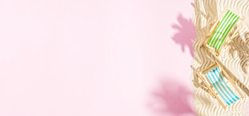 Two mini deck chairs on sand with palm tree shadow on pink background, summertime concept, copy space, top view