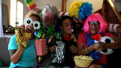 Group of friends supporters excited exult during a football match on tv. Family people watching world cup on television and have fun together exulting for the score. Mixed ages and sport channel