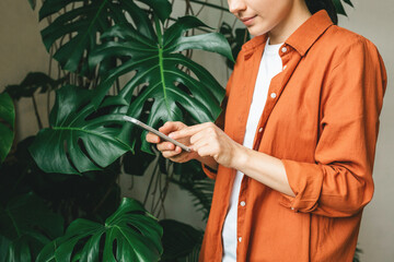 Close-up of a young woman typing, chatting, writing a message on her phone, at home in a green garden with plants. The concept of remote work or training. 