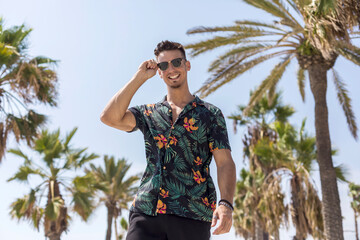 College student wearing flowered shirt, black shorts, sunglasses, walking on walkway