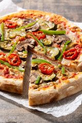 Vegetarian pizza with zucchini, tomato, peppers and mushrooms on wooden table	