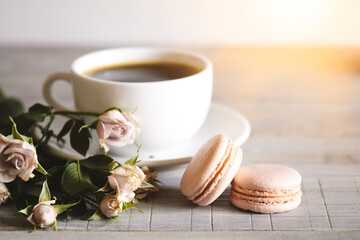 Macaroons on a wooden table with cup of coffee and flowers.