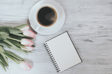 Holiday and celebration. Top view of pink tulips, coffee cup and notebook on white wood background, flat lay