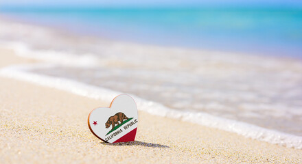 Fototapeta na wymiar Flag of the state of California in the shape of a heart on a sandy beach. The concept of the best vacation in California resorts