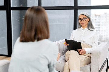 Senior grey haired therapist expresses support and empathy to a upset female patient during therapy session. Mental health concept