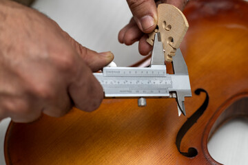 Hands of an unrecognizable Latin American luthier taking precise measurements of a violin bridge...