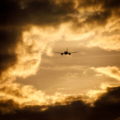Silhouette of an airplane flying at sunset clouds.