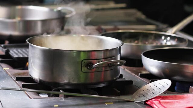Water steam coming from a boiling casserole, surrounded by cooking pans in professional and commercial kitchen at a high cuisine restaurant