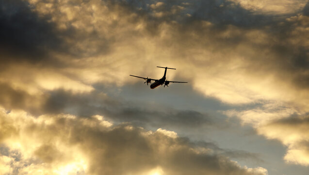Silhouette of an airplane flying at sunset clouds.