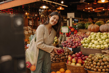 Smiling caucasian young woman looking around local food market during day. Brunette looks at camera, wears casual clothes. Ecological products concept