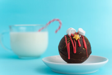 Chocolate bomb with marshmallows and Christmas decorations on a white plate against a blurred image...