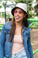 Portrait of a young woman standing outdoors and looking at the camera through sunglasses.