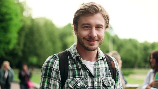 Portrait of student guy standing with books near the park and looking at the camera. Portrait of attractive blond man. 