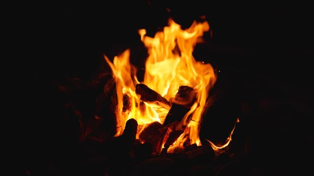 Slow motion of wood burning in the bright flames of a campfire. Night campfire. A camping spot on a wild pebble beach while traveling