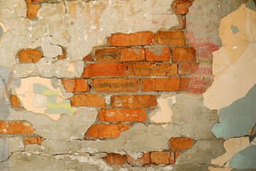 An old red brick street wall.The worn facade of the building with damaged light plaster.Copyspace.