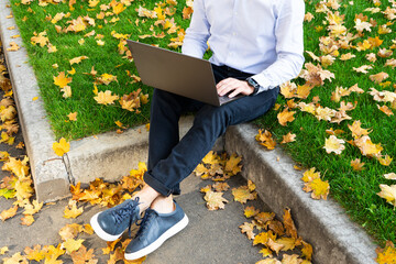 Young man using laptop in the park. Autumn park and people.