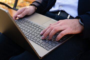 Young man using laptop in the autumn park, close-up. Businessman in laptop.