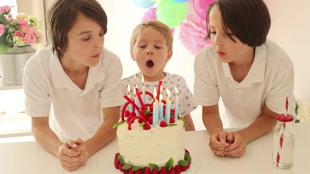 Cute child, preschool boy, celebrating birthday at home with homemade cake with raspberries, mint and candies, balloons and decoration in the room