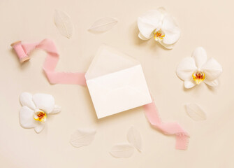 Wedding envelope near white orchid flowers and silk ribbons on yellow, mockup