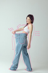 Portrait of slim woman in underwear wear posing in giant oversized jeans isolated over gray studio...