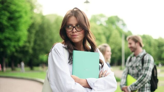 Jealous brunette student girl watching her friend flirting with guy she likes. Unhappy girl in the campus park.