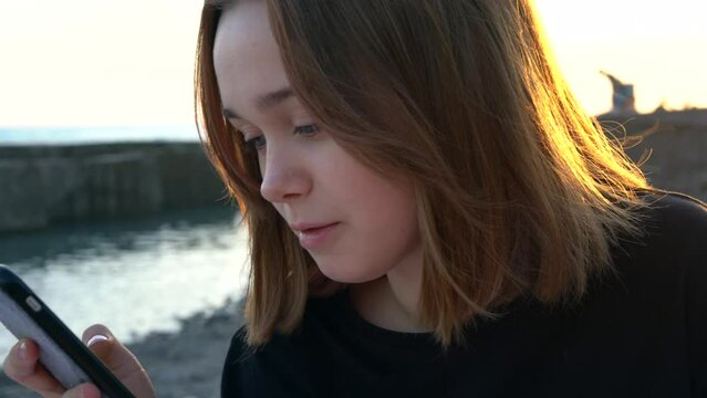 Portrait of a Young Woman Using Mobile Phone on the Beach at Sunset Time. 
