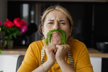 concept of positive lifestyle, Humor healthy food, Funny young woman using dill as mustache in...
