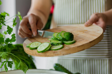  woman slices cucumber for salad on wooden background, unrecognizable person, cooking at home