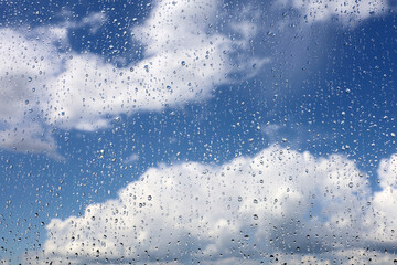 Raindrops on the window glass on blurred background of sky with white clouds. Beautiful water...