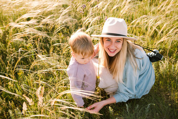Blond happy mother in hat with camera hug her son among field, look at camera, smile