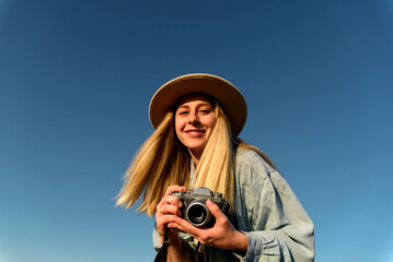 Blond happy female photographer in hat look at camera on blue sky background