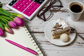 holiday in financial sphere, view of desktop surface tulips coffee with cake and notepad with calculator on wooden light background close-up