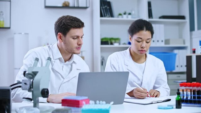 Male and female researchers checking test results on laptop, writing report