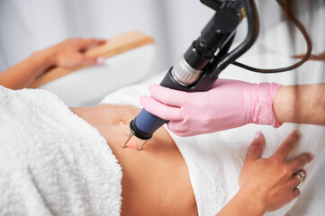 Close up view of working element of laser skin resurfacing machine. The beautician's hand purposefully treating the patient's abdomen, stimulating local skin rejuvenation.