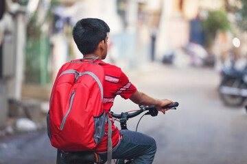 Indian teenage boy with backpack riding bicycle on city street