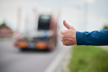 Fototapeta Close up of man's hand hitchhiking by roadside. Male hand showing thumbs up gesture outdoors on blurred background. Hitchhiking, hitching, auto stop concept. obraz