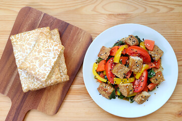 Stack of fresh Tempeh and colorful vegetables salad with roasted Tempeh cubes on wooden table