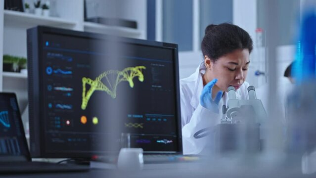 Professional lab technician studying sample under microscope scientific research