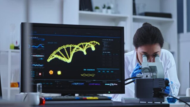 Female lab assistant looking into microscope, writing scientific test results