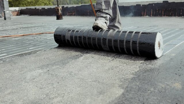 Worker mounts on flat roof, vapor barrier made of bituminous membrane welded with flame burner