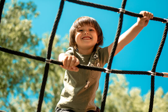 A child climbs up an alpine grid in a park on a playground on a hot summer day. children's playground in a public park, entertainment and recreation for children, mountaineering training.