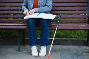Blind man reading braille book, sitting on bench in summer park, resting - obrazy, fototapety, plakaty