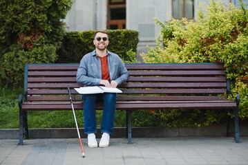 Blind man reading book on bench in park