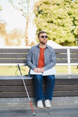 Blind man reading braille book, sitting on bench in summer park, resting