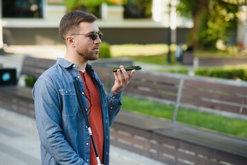 Young blind man with smartphone sitting on bench in park in city, calling.