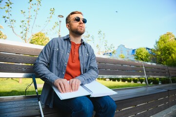 Blind man reading book on bench in park